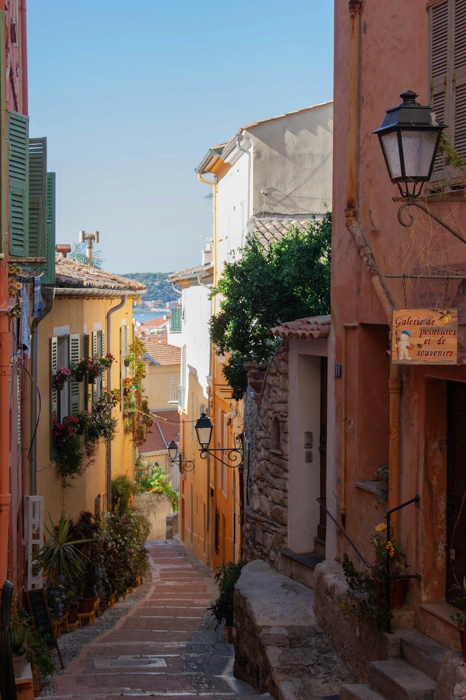 Cobblestone alleyway with historic buildings sloping down toward the ocean.