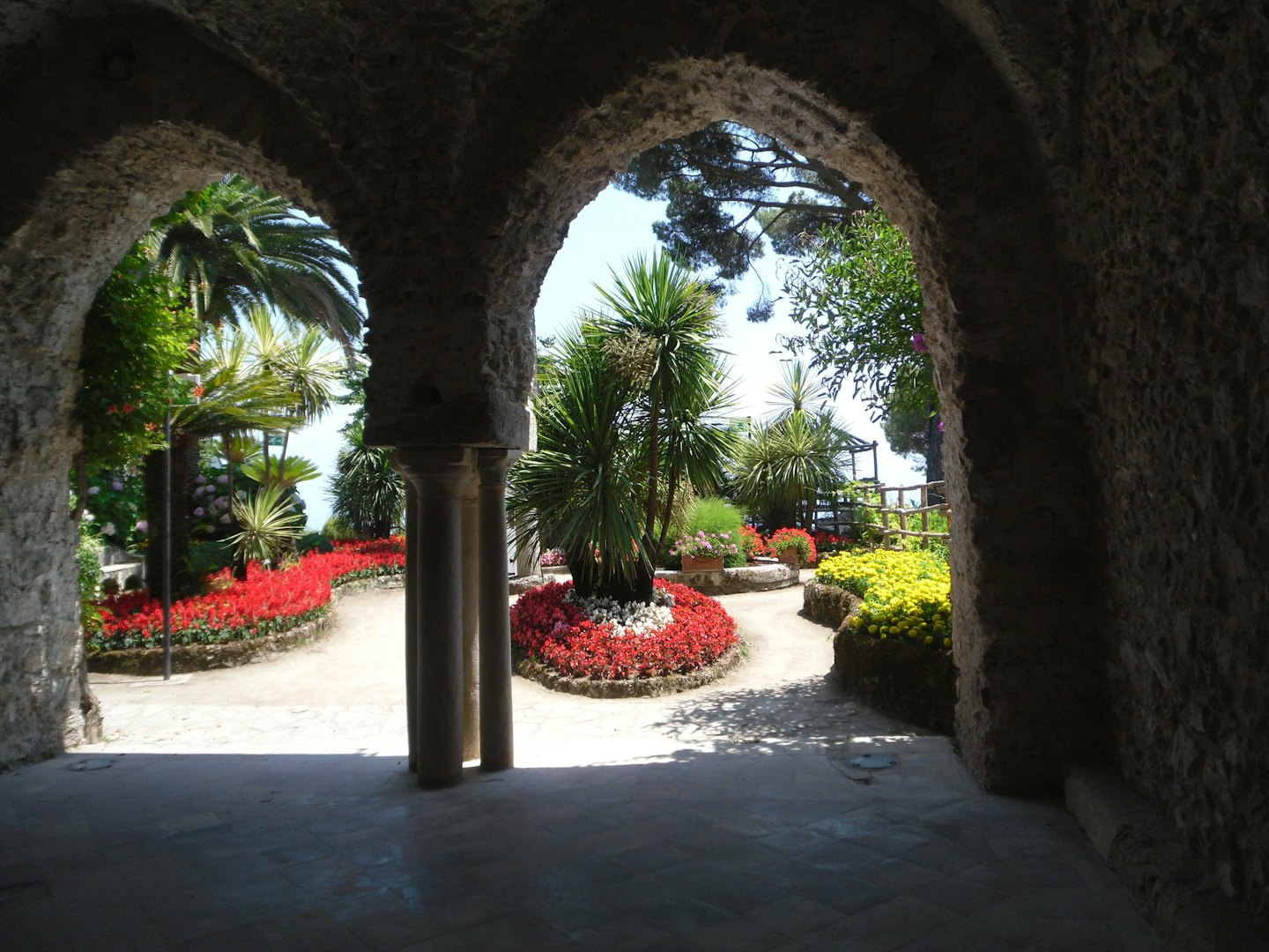 Sunlit garden viewed through ancient stone arches.